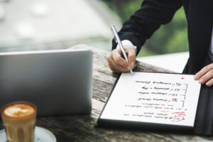 A person sitting next to a laptop, putting together an implementation plan on paper.