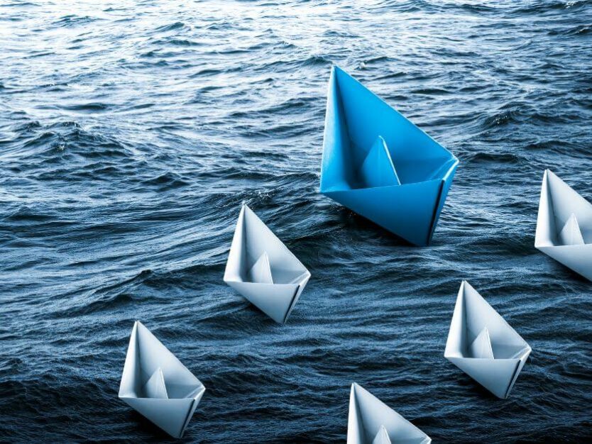 The 4 R's of the Leadership Journey - Risk, Rejection, resilence, Reinvent. Blue paper boat leading the grey boats in water